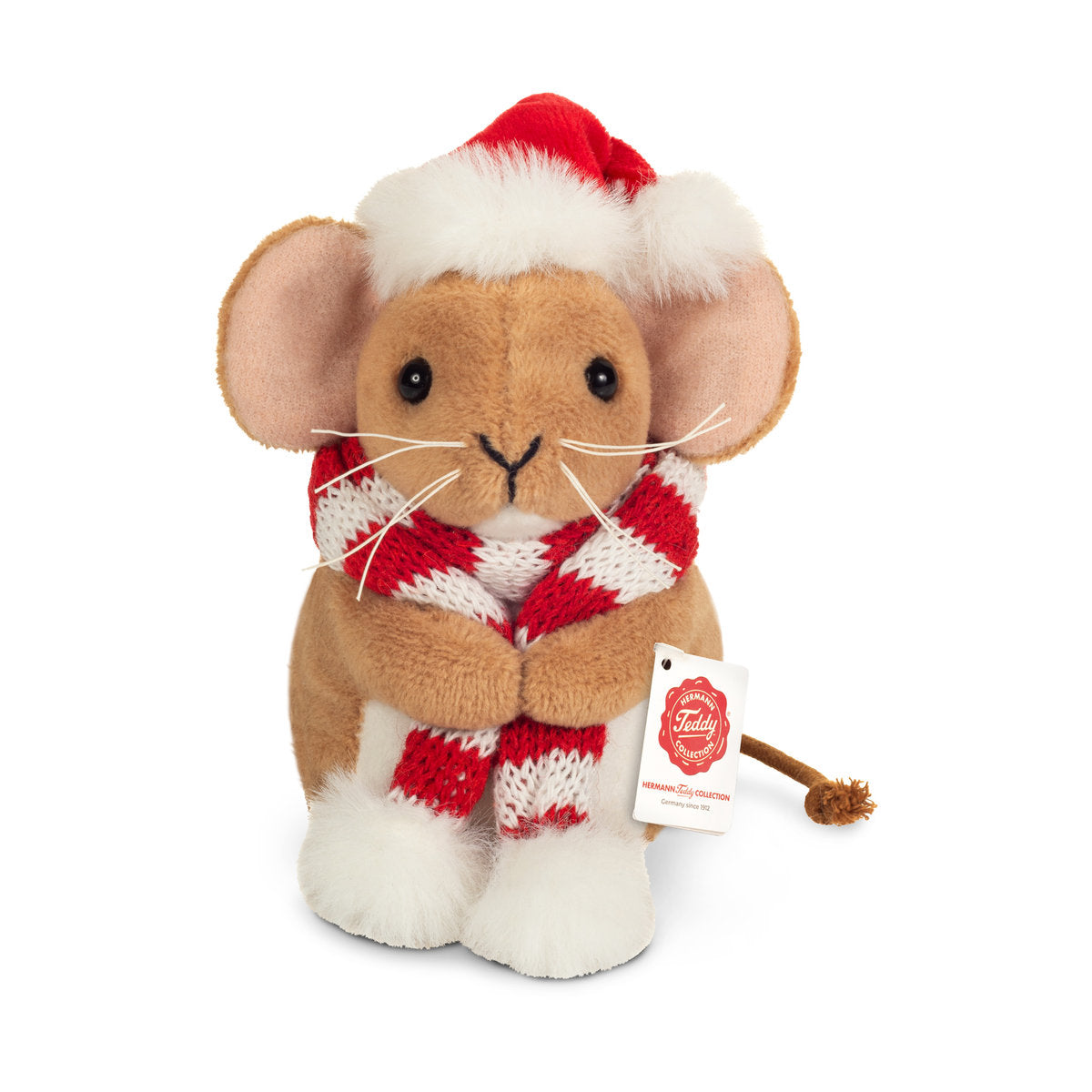 This is Small Christmas Mouse With Scarf by Teddy-Hermann. Sitting mouse with short, dense beige fur that has a slight sheen; white fur is visible on the front of the tummy and the tops of the feet and is short and fluffy. Muzzle is beige with long white whiskers; inner ears are pale pink. Eyes are black and round. Nose is black and V-shaped. Tail is thin and brown with a knotted end. A red Santa hat with white fluffy trim sits on the head and a red-and-white striped knitted scarf is wrapped around the...