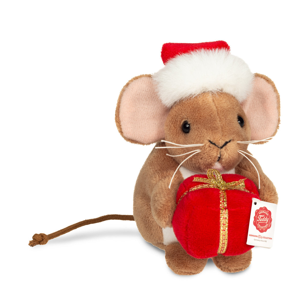 This is Small Christmas Mouse With Present by Teddy-Hermann. Small brown mouse sitting upright holding a present. The fur is brown, short, smooth and with a slight sheen; the tummy is white and the inner ears are pink. Eyes are black and round. Nose is black and small and triangular. Whiskers are white and long. Ears are large and rounded, matching the brown fur at the outer ear. Paws are brown and match the fur; paw pads are not visible. A long thin brown tail extends behind. The mouse wears a red San...