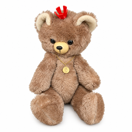 This is DDR Berlin Bear by Japanese. This fully jointed bear sits upright and cannot balance to stand. The fur is brown, medium length, slightly shaggy with a soft sheen. Inner ears, muzzle and tummy are beige and appear short and dense compared with the rest of the fur; paw pads are not visible. Eyes are black and round. Nose is pale yellow and oval with a black vertical line. There are no additional markings except lighter beige inner ears and tummy. Accessories visible are a red plastic crown perche...