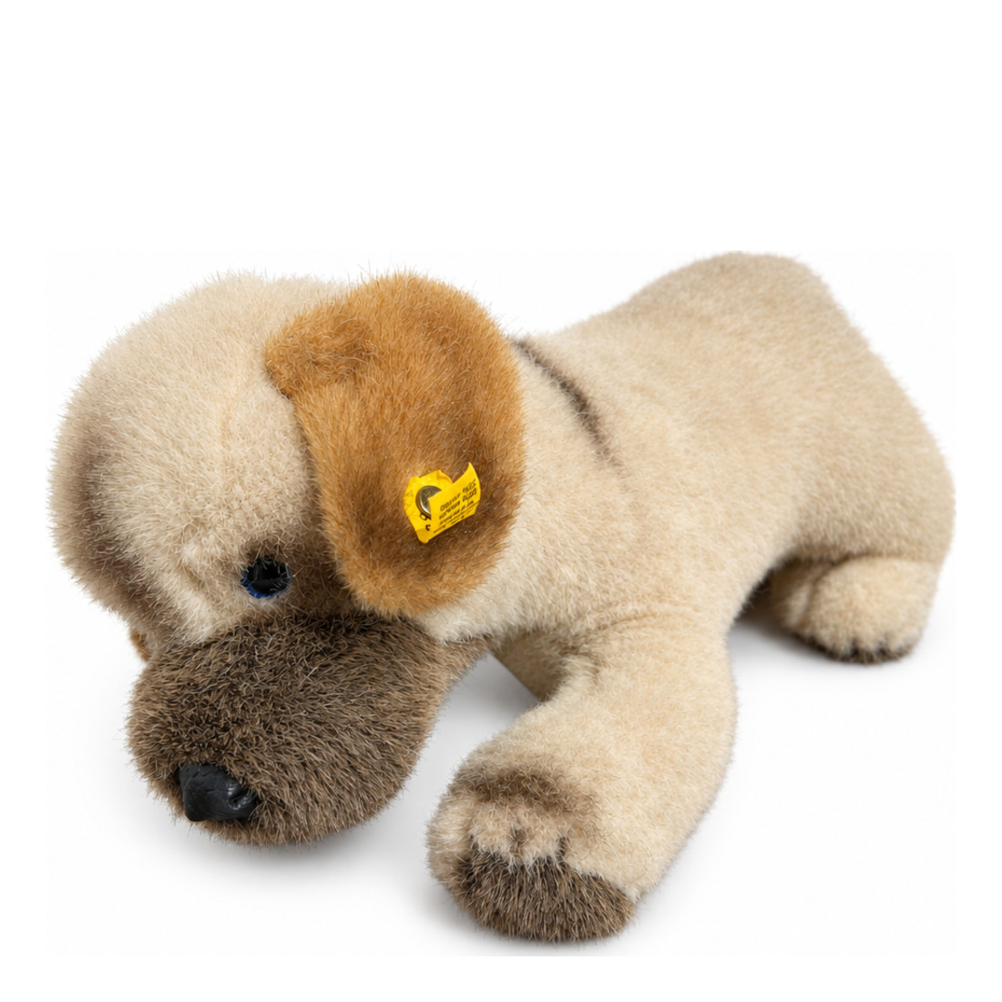 This is Welfo by Steiff. Welfo is a standing dog with short, dense plush fur that has a slight sheen. The fur colours are beige over most of the body and medium to dark brown on the muzzle, ear tops and paw tips; a narrow darker brown stripe runs along the back. The muzzle is dark brown, the inner ears are brown, the tummy is beige, the paws are beige with brown tips and the visible paw pads are brown. The eyes are blue and the nose is black and rounded. There are no garments or accessories visible. Th...